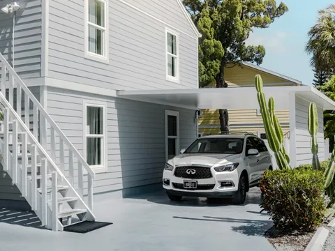 Carport aluminium blanc à toit plat le long d’une maison à bardage clair entourée de cactus, SUV garé dessous