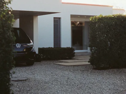 Carport aluminium à toit plat en porte-à-faux devant une villa contemporaine blanche, allée en gravier au crépuscule