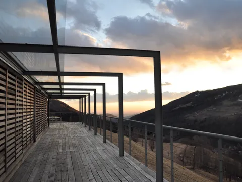 Terrasse couverte par une pergola aux lames orientables en aluminium, vue sur la montagne au coucher du soleil