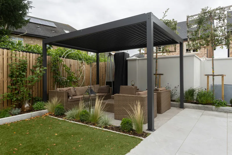 Salon de jardin sous une pergola bioclimatique anthracite avec mobilier en résine tressée